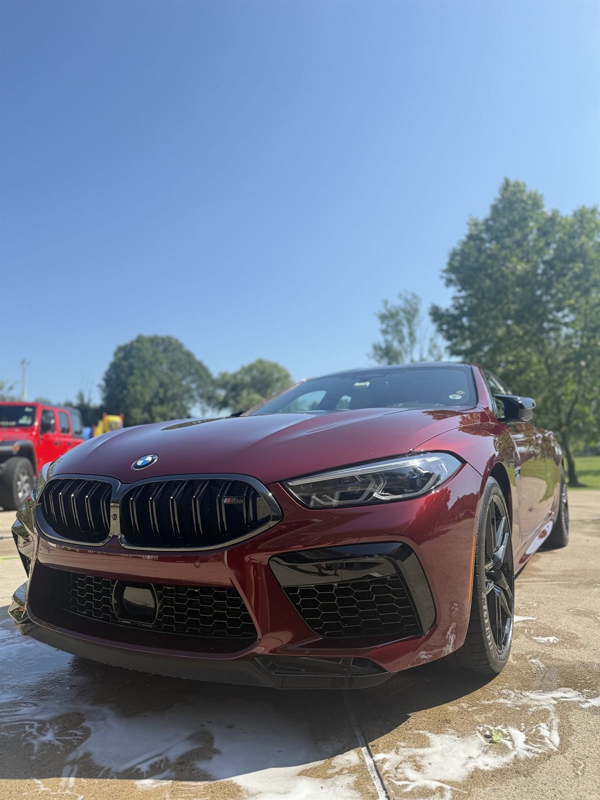 Burgundy BMW M8 mid-wash, covered in foam during an exterior detail